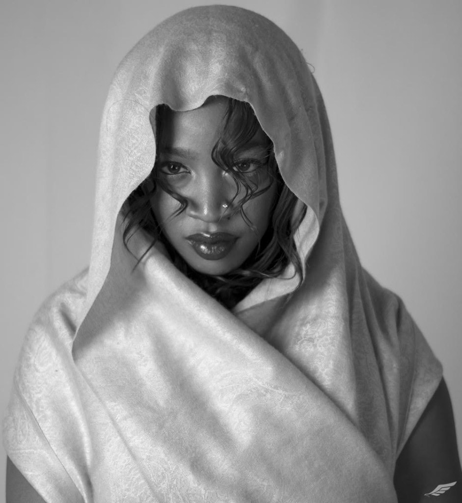 Black and white portrait of a woman wrapped in a pale patterned shawl, wet curls across her face