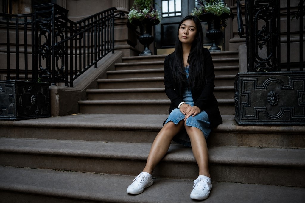 Woman in a black blazer and denim dress sitting on brownstone steps between black iron railings